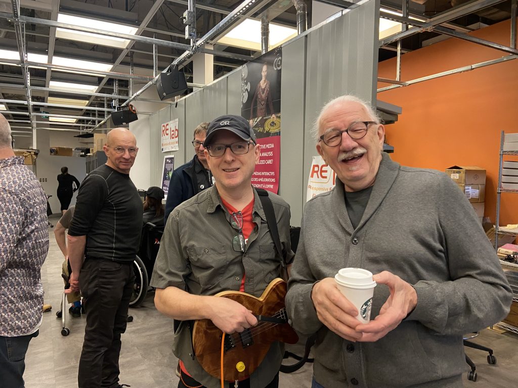 A group of people standing and smiling in the picture, showing friendship. One of which was holding an electronic guitar.