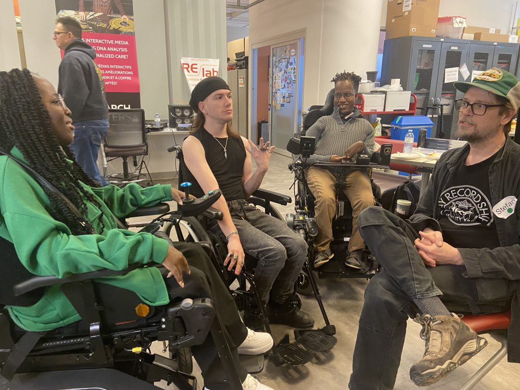 Miss Jacqui, Dyllan Lambert Monroe, Gift Tshuma, and Stefan sitting in a circle in Re/Lab, smiling and talking with each other.