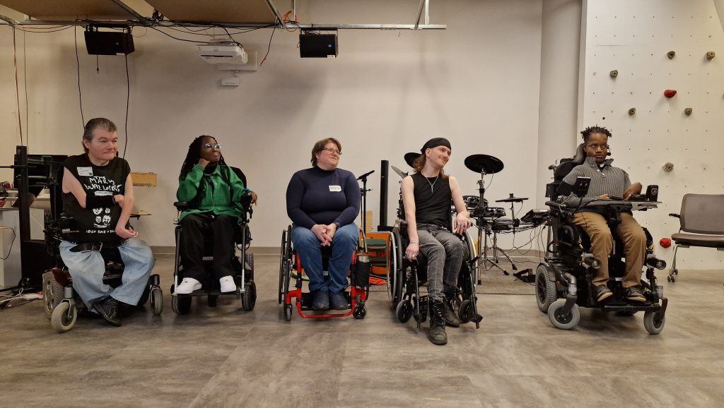 John Kelly (he/him), Miss Jacqui (she/her), Diane Kolin (she/her), Dyllan Lambert Monroe (they/them), and Gift Tshuma (he/him) sitting side by side in Re/Lab, facing their left direction.