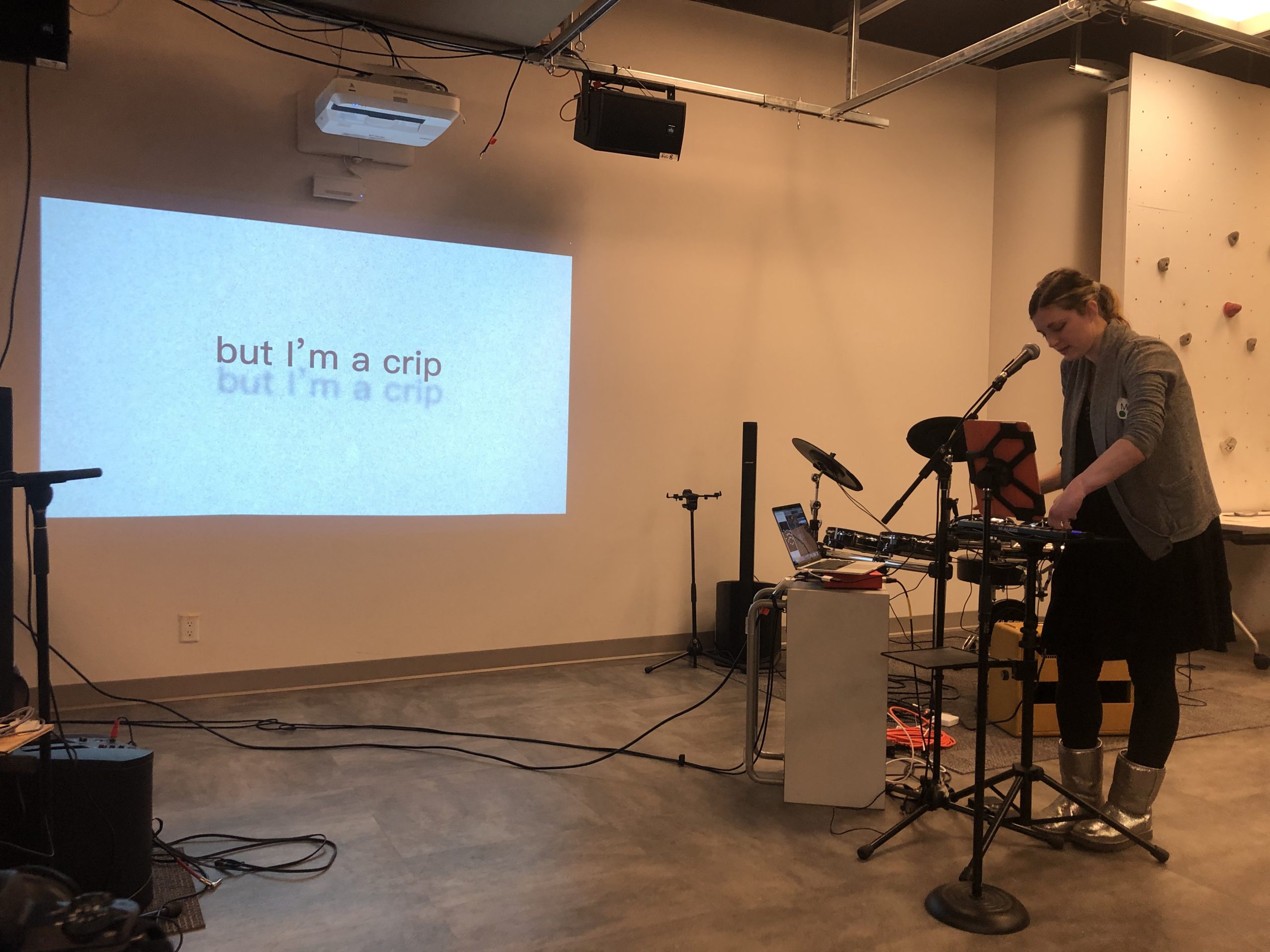 Molly Joyce standing in Re/Lab, singing with a microphone, while using a laptop, an iPad, and a mini MIDI keyboard to perform music.